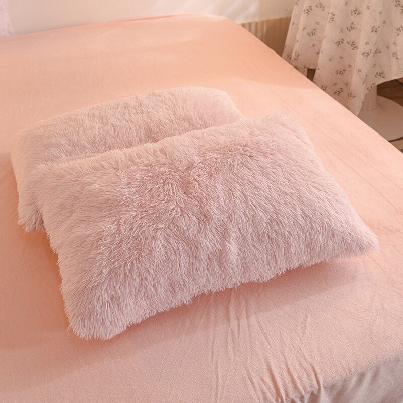 Foto van 2 roze fluffy fleece kussen slopen op een bed.